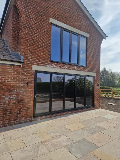 Anthracite bifolds closed in a red brick gable, matching window above, new sandstone patio