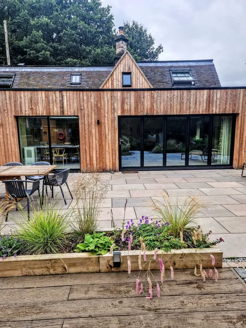 Black aluminium bifolds, closed, in a timber-clad extension above a sandstone terrace and planted bed