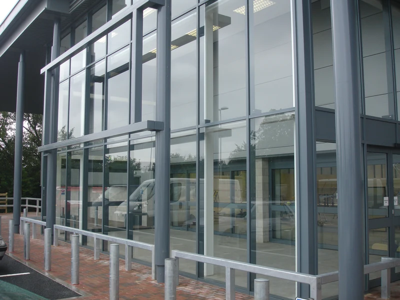Grey aluminium curtain walling to a commercial unit, bollards and car park outside