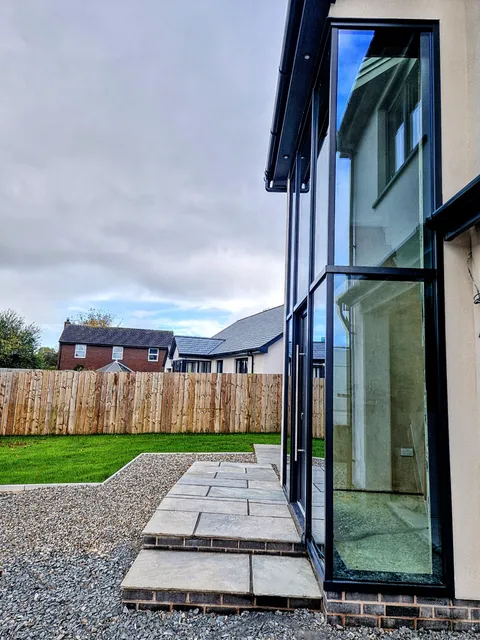 Corner of a full-height anthracite aluminium glazed screen seen from outside, across a lawn