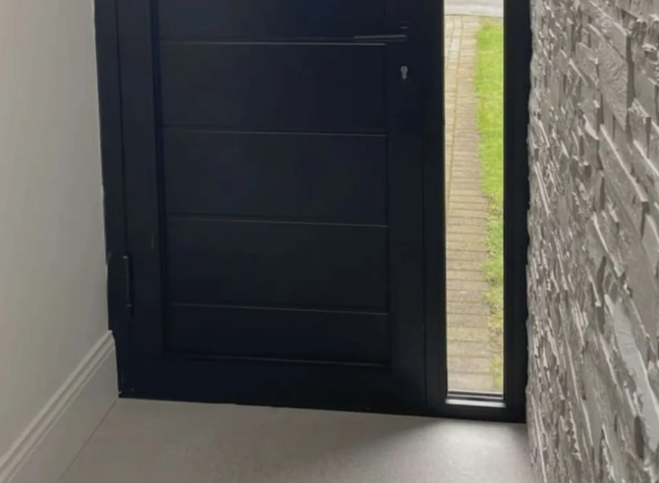 Anthracite aluminium front door, closed, with a full-height glazed sidelight, seen from a stone-clad hallway