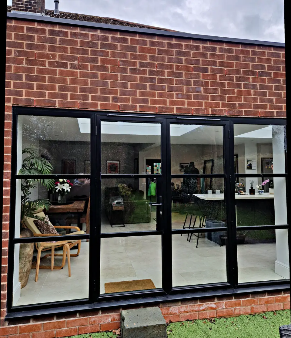 Black Crittall-style aluminium French doors with fixed side panes, closed, in red brickwork