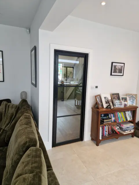 Black steel-look internal door, closed, between a living room and a stair hall; clear glazing, one low bar
