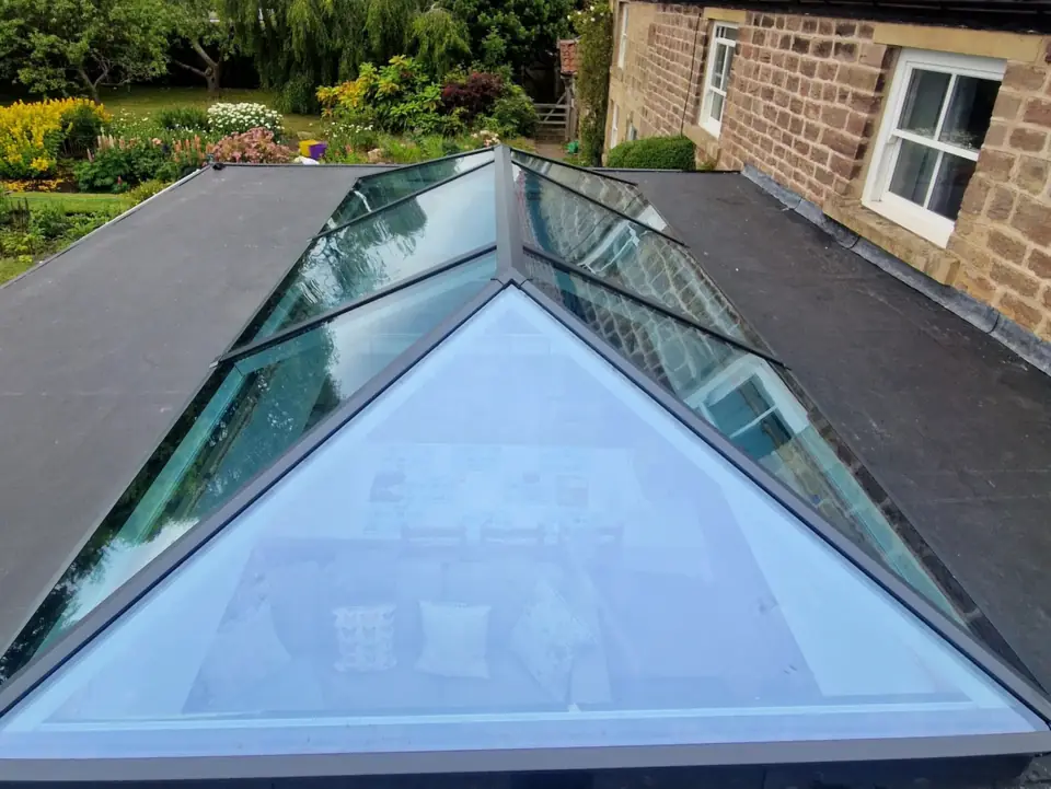 Aluminium roof lantern on a flat-roofed extension, seen from above, with a stone house and garden beyond